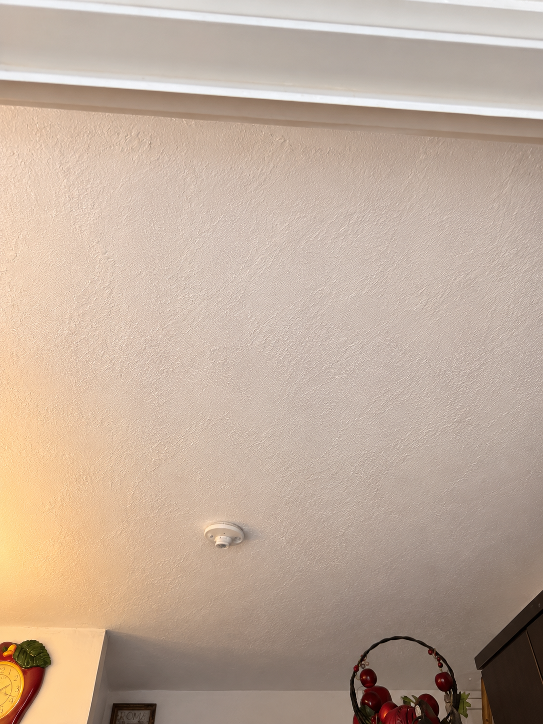 Ceiling with smoke detector and part of kitchen decoration including a colorful fruit basket.