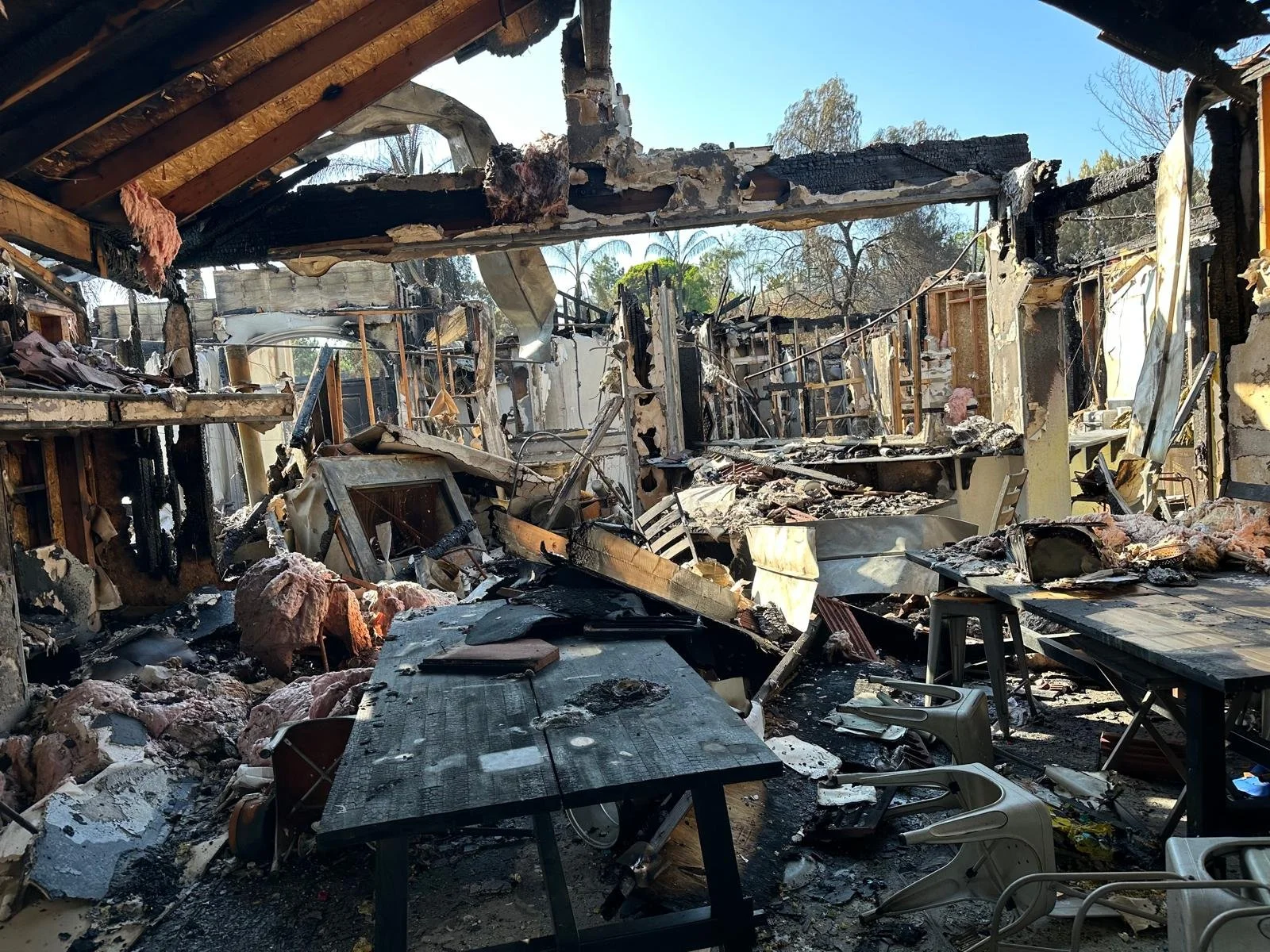 Burned and damaged interior of a house with debris, blackened walls, and furniture, showing aftermath of a fire.