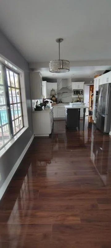 Modern kitchen with white cabinets, stainless steel appliances, and a large window. Features a wooden floor and a chandelier hanging from the ceiling.
