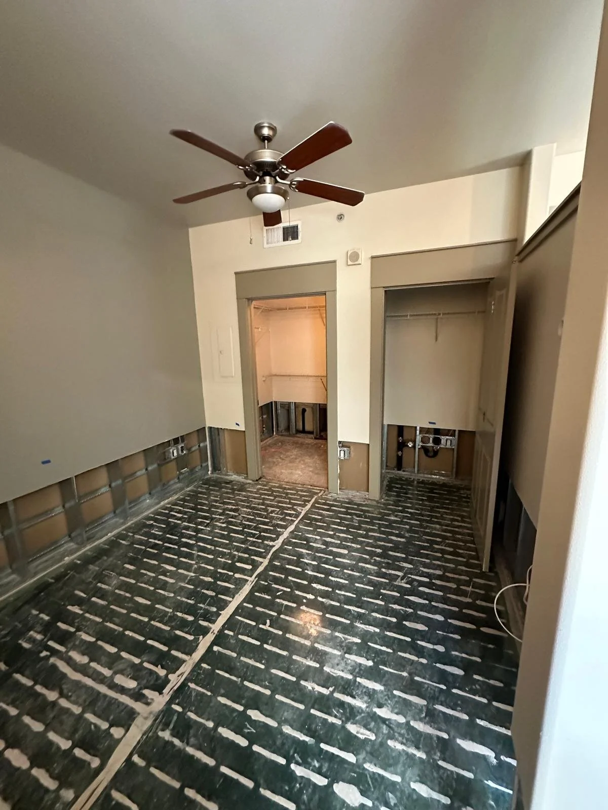 Room under renovation with exposed wall studs, black flooring with white markings, and a ceiling fan.
