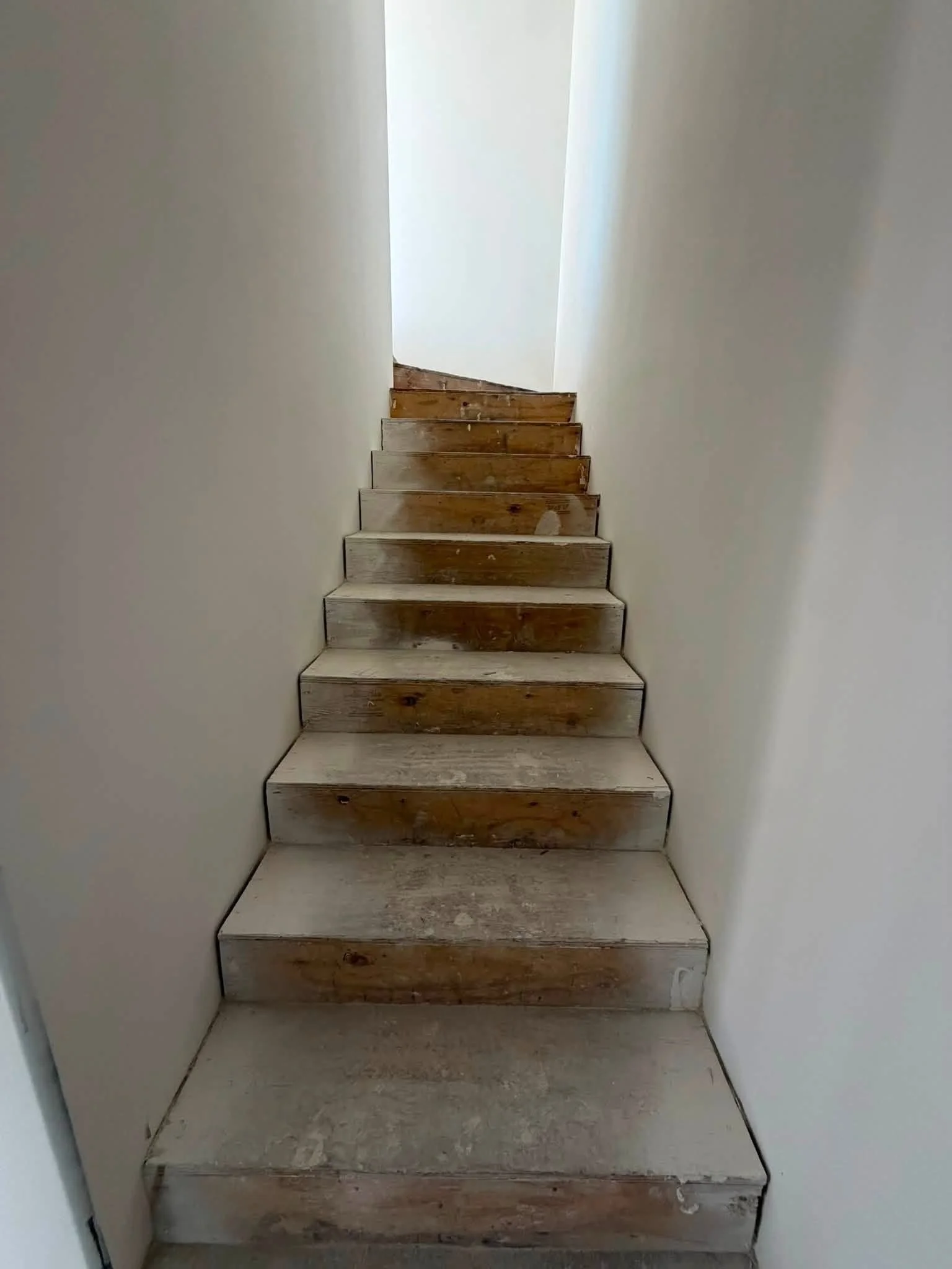 Wooden stairs leading up to a closed white door at the top, enclosed by white walls.