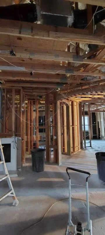 Interior view of a house under construction with exposed wooden framing, construction tools, and temporary lighting.