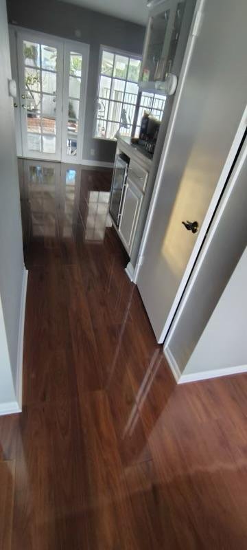 Interior view of a room with wooden flooring, white walls, a windowed door, and a small kitchen area with cabinets and appliances.