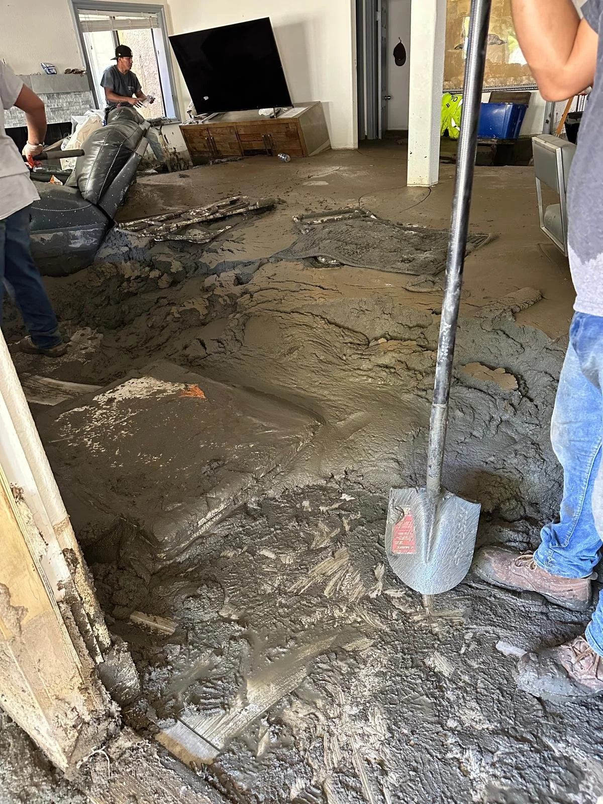 Moving mud and debris inside a house after flood, with a shovel and workers cleaning up.