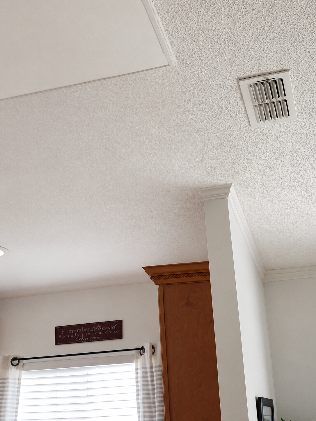 Ceiling with air vent and part of a collage wall art in a living room.