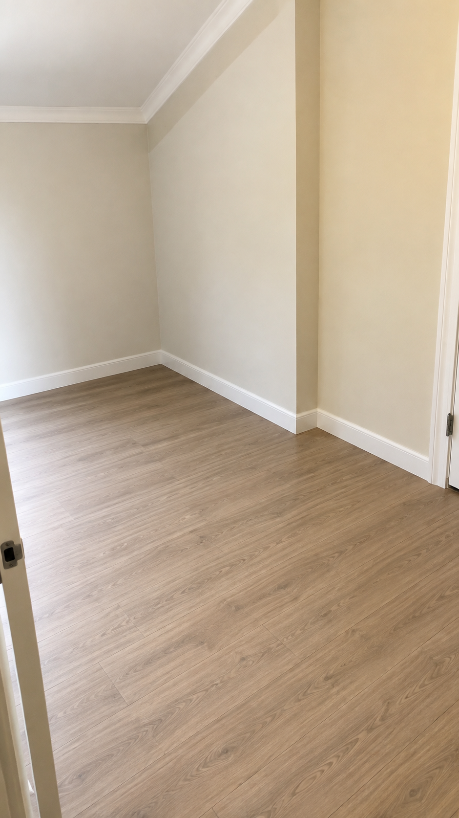 Empty room with light wood flooring, white walls, and white baseboards, with an angled ceiling on the left side.