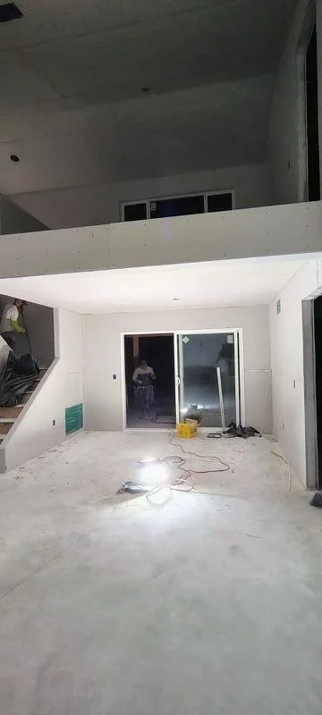 Construction site of a modern house interior with an open floor plan, unfinished concrete floors, and large glass sliding doors.
