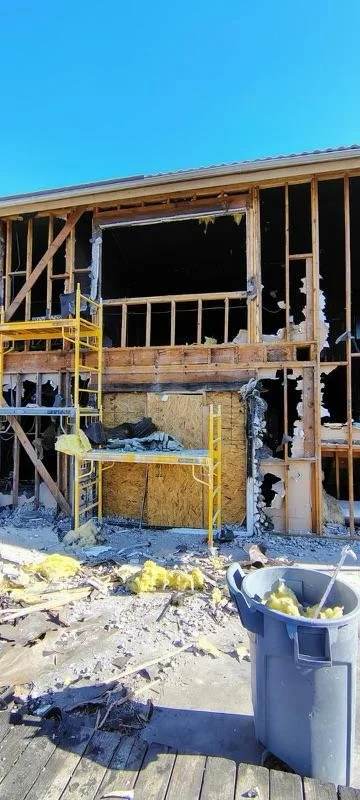 Building under construction with exposed wooden framing, scaffolding, and construction debris on the ground.