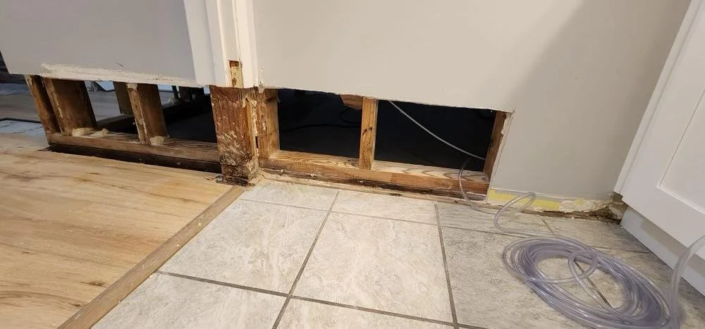 Kitchen with a missing cabinet panel, exposing the interior wall and plumbing, with some tubing on the floor.
