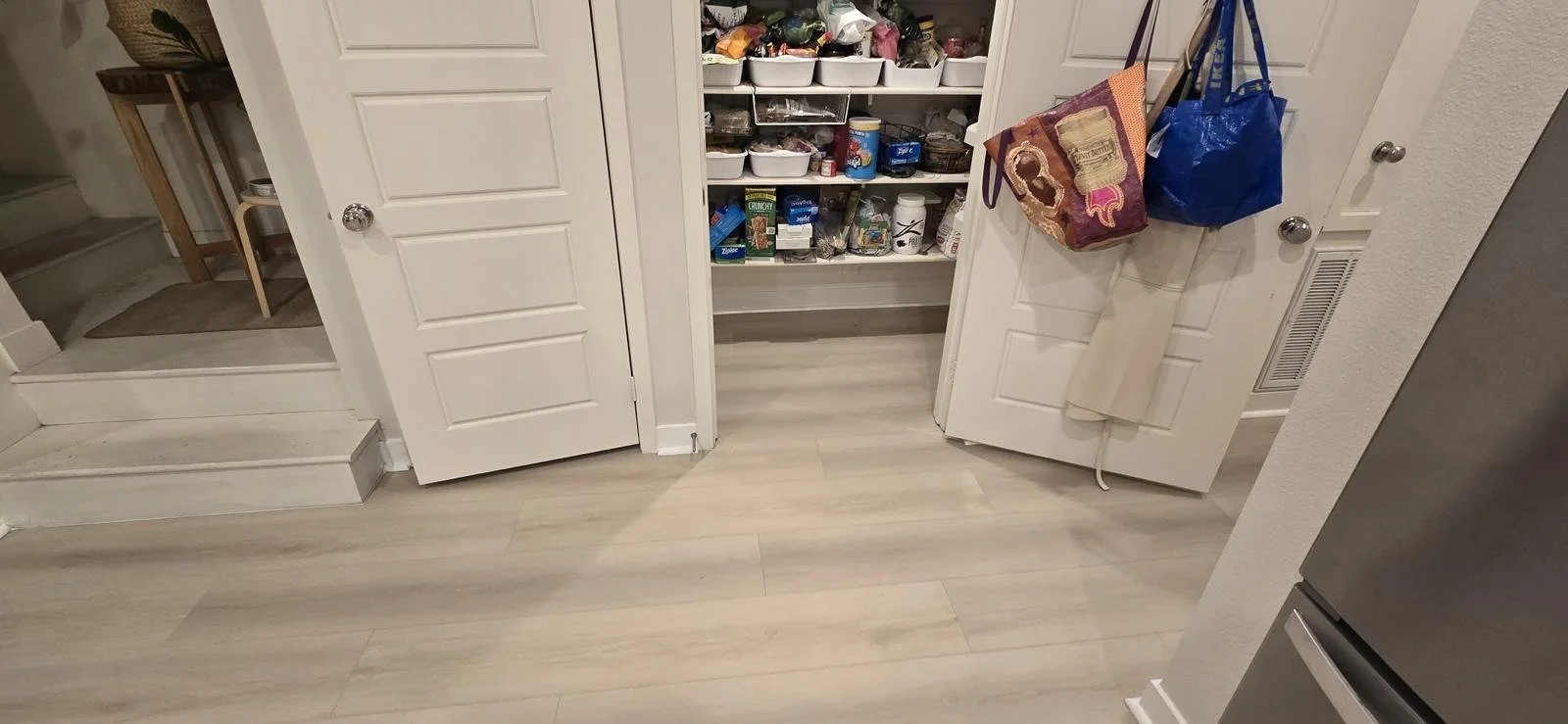 Open pantry closet with various food items, snacks, and containers, with bags hanging on the door.