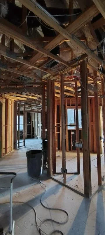 Interior of a building under construction with exposed wooden framing, wiring, and open spaces for rooms and windows.