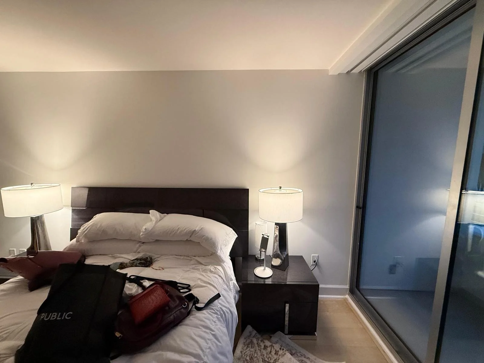A bedroom with a bed, lamps on either side, and a sliding glass door to a balcony.