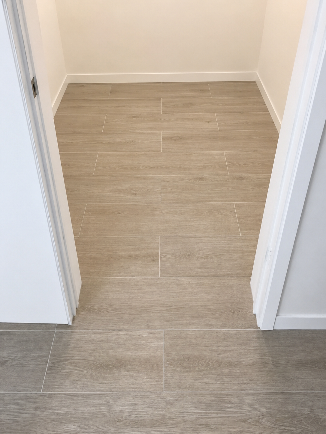 View of an empty room with beige wood-look tile flooring and white walls.