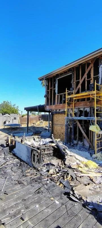 Construction site with a damaged building, scaffolding, debris, and a partially destroyed roof.