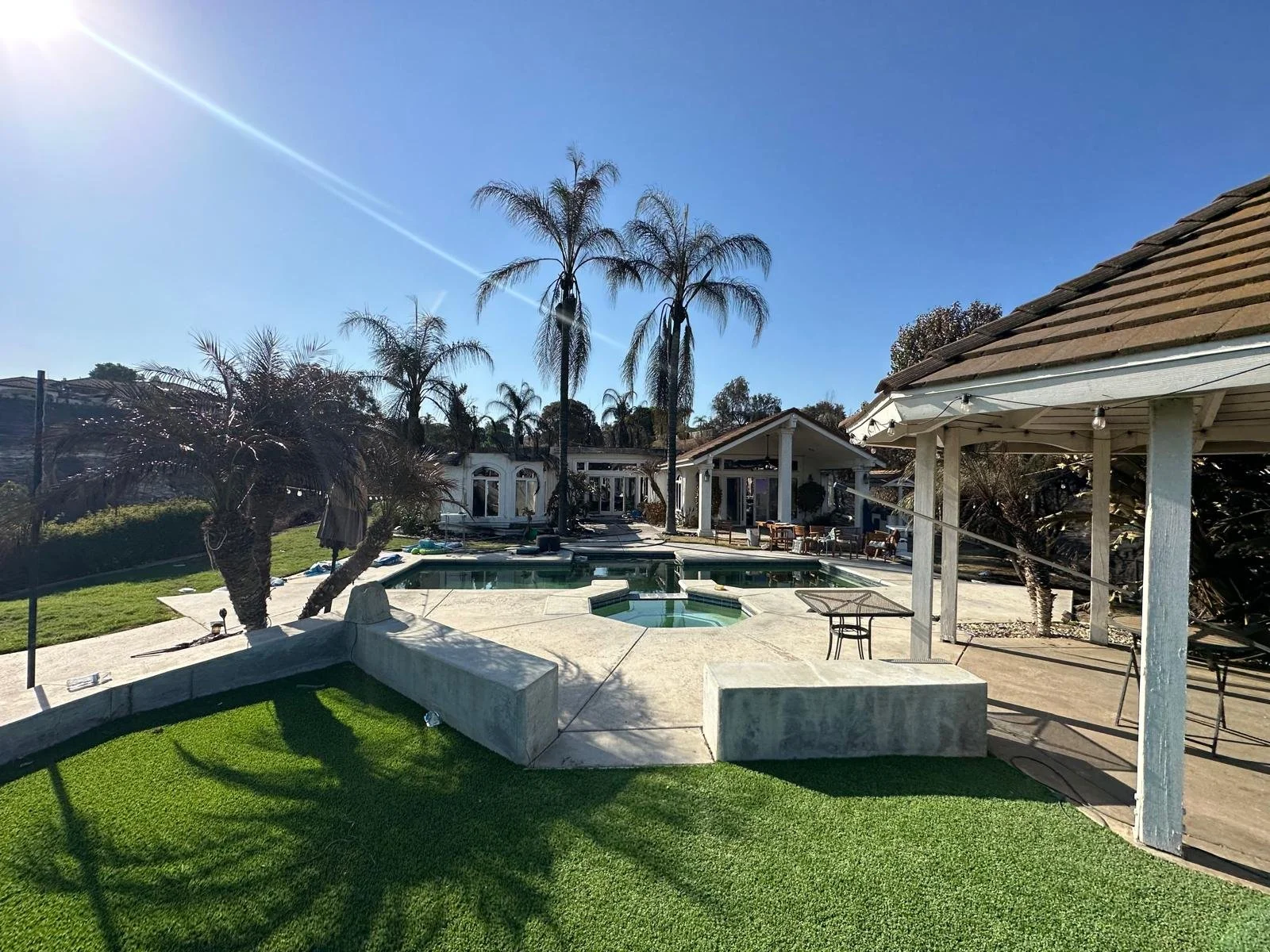 Backyard with pool, palm trees, and a small building under a clear blue sky.
