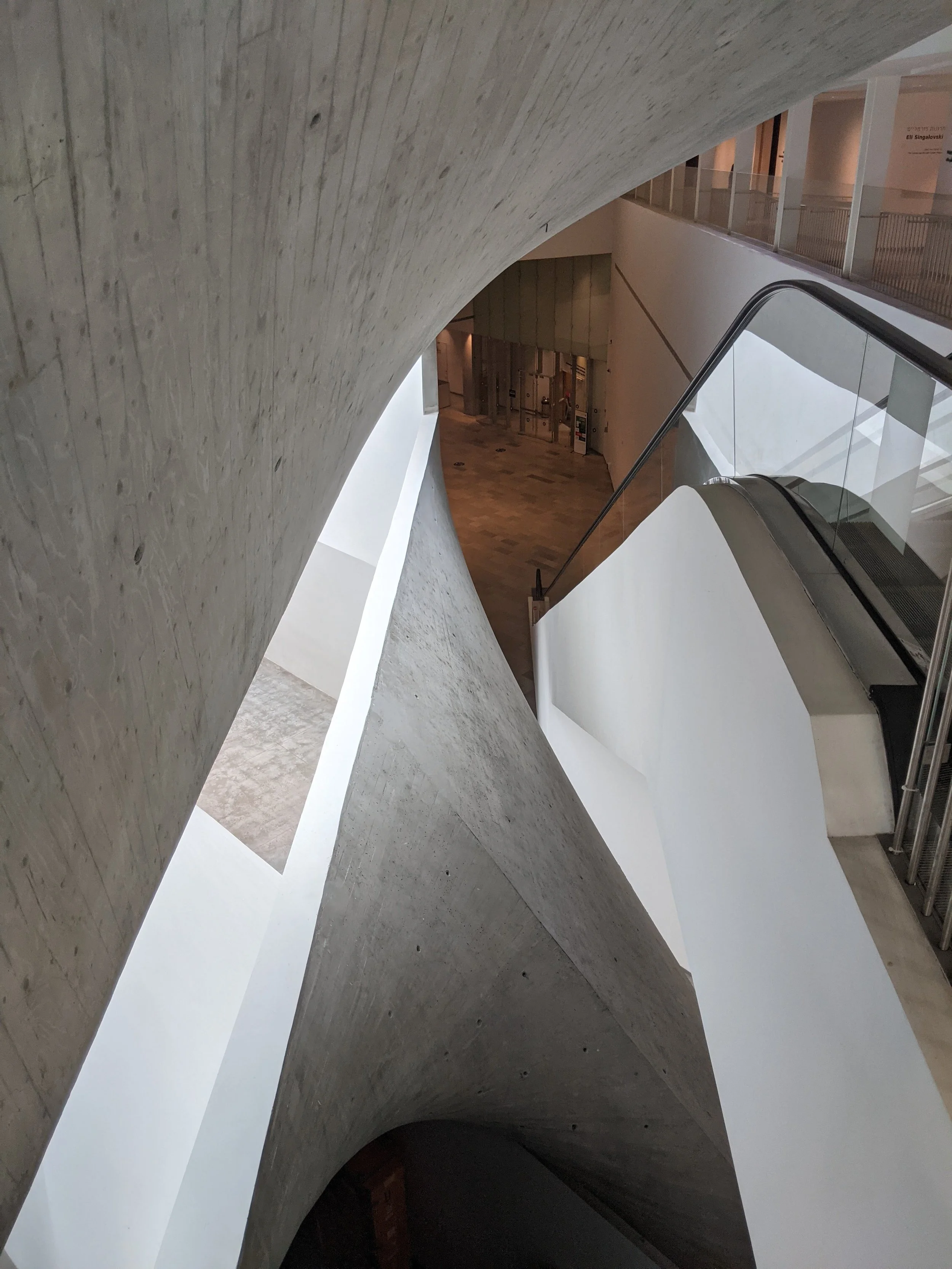 Interior view of a modern building with curved concrete walls, white staircases, and glass railings.
