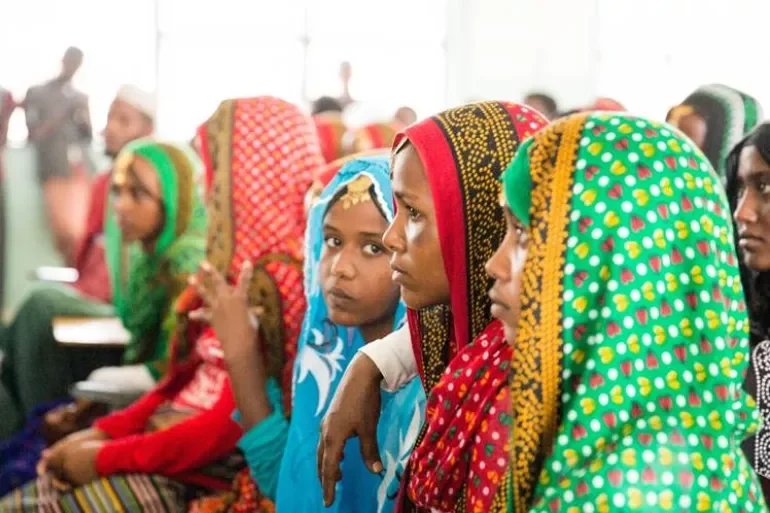 Group of women wearing colorful traditional headscarves sitting attentively in a bright indoor setting.