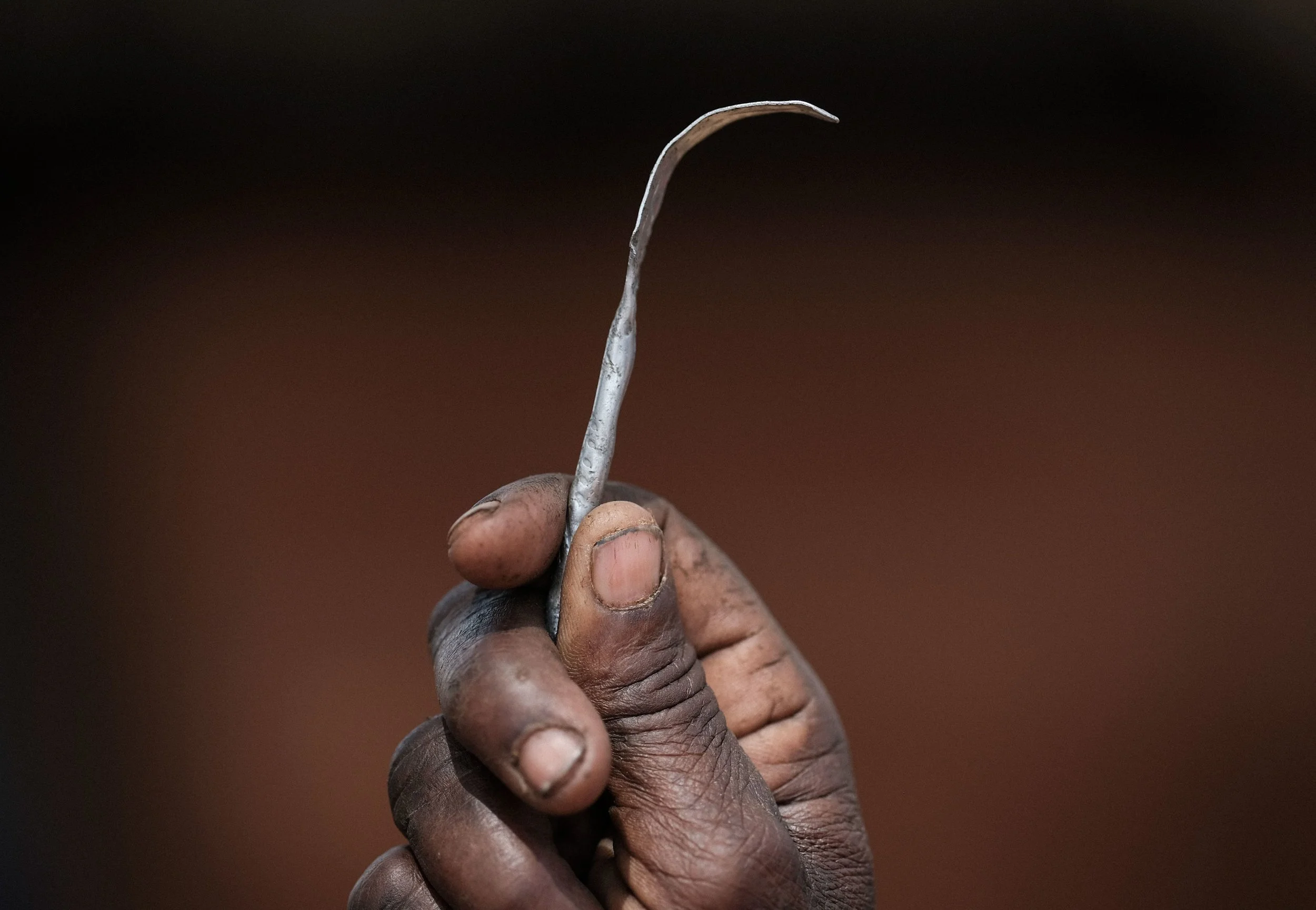 Close-up of a person's hand holding a small, curved metal tool against a dark background.