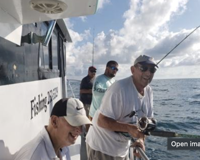 Group of men fishing from a boat at sea on a partly cloudy day, smiling and holding fishing rods.