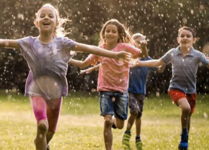 Children running and playing in a field, splashing water, enjoying outdoor summer activities.