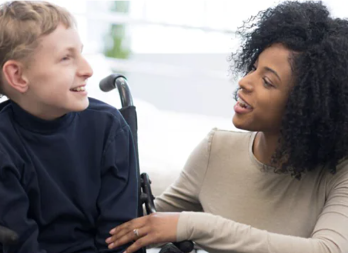 A woman talking and smiling at a boy in a wheelchair.