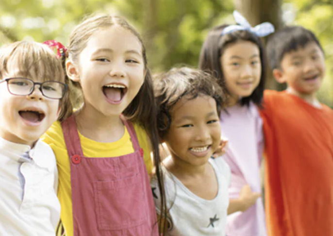 Group of five diverse children outdoors smiling and posing for the camera.