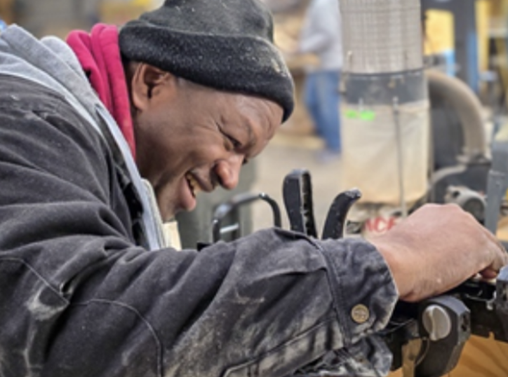 A man smiling and working on a machine in a workshop or industrial setting.