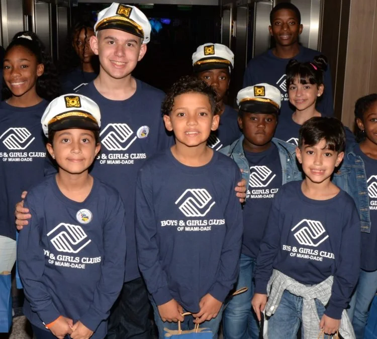 A group of boys and girls at a Boys & Girls Clubs of Miami-Dade event, wearing matching navy blue shirts and some in white captain's hats.