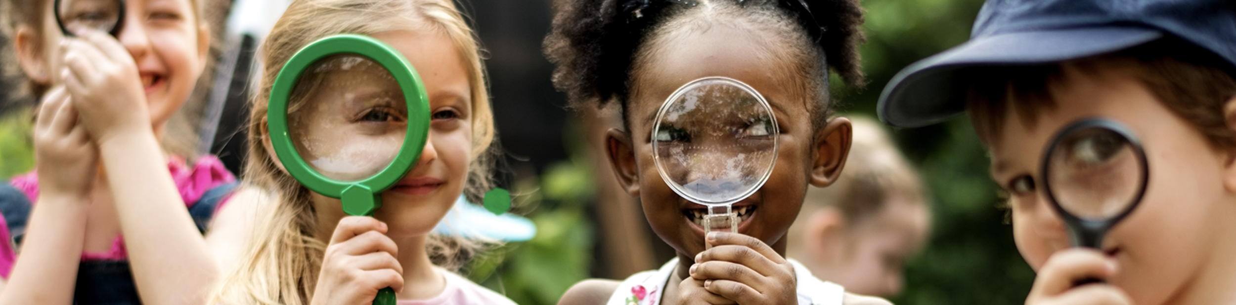 Children outdoors using magnifying glasses to observe something closely.