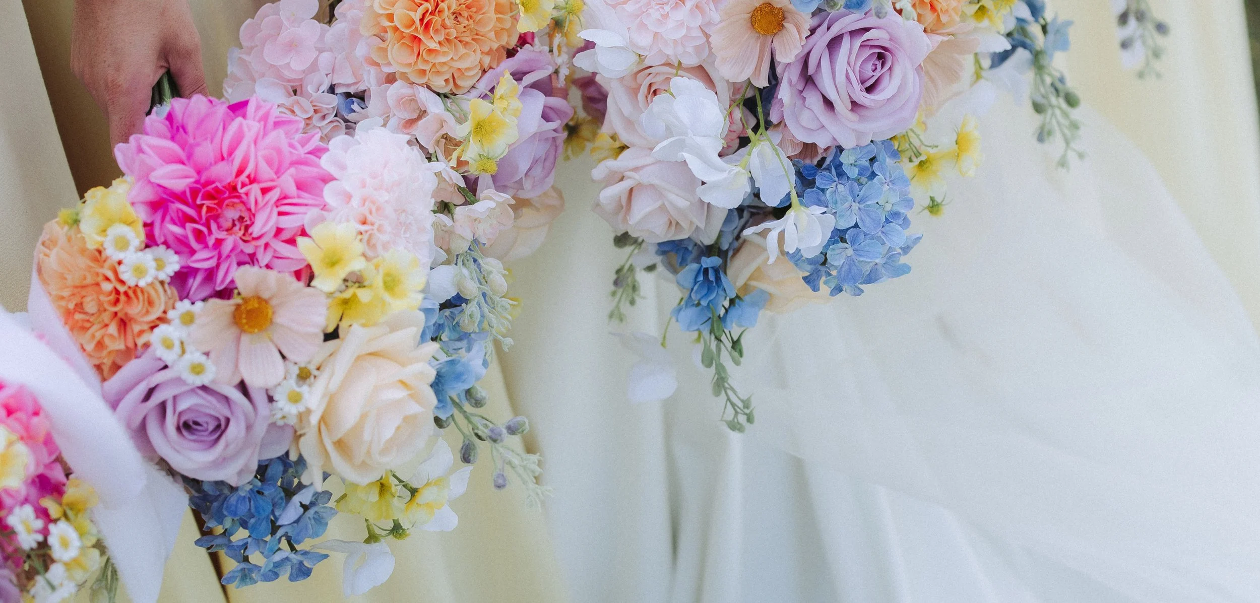 A person holding a colorful bouquet of flowers consisting of pink, purple, yellow, white, and blue blossoms.