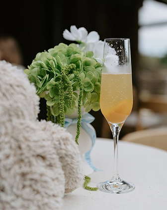 A champagne flute filled with a sparkling drink next to a white vase with a bouquet of green hydrangeas and white flowers.