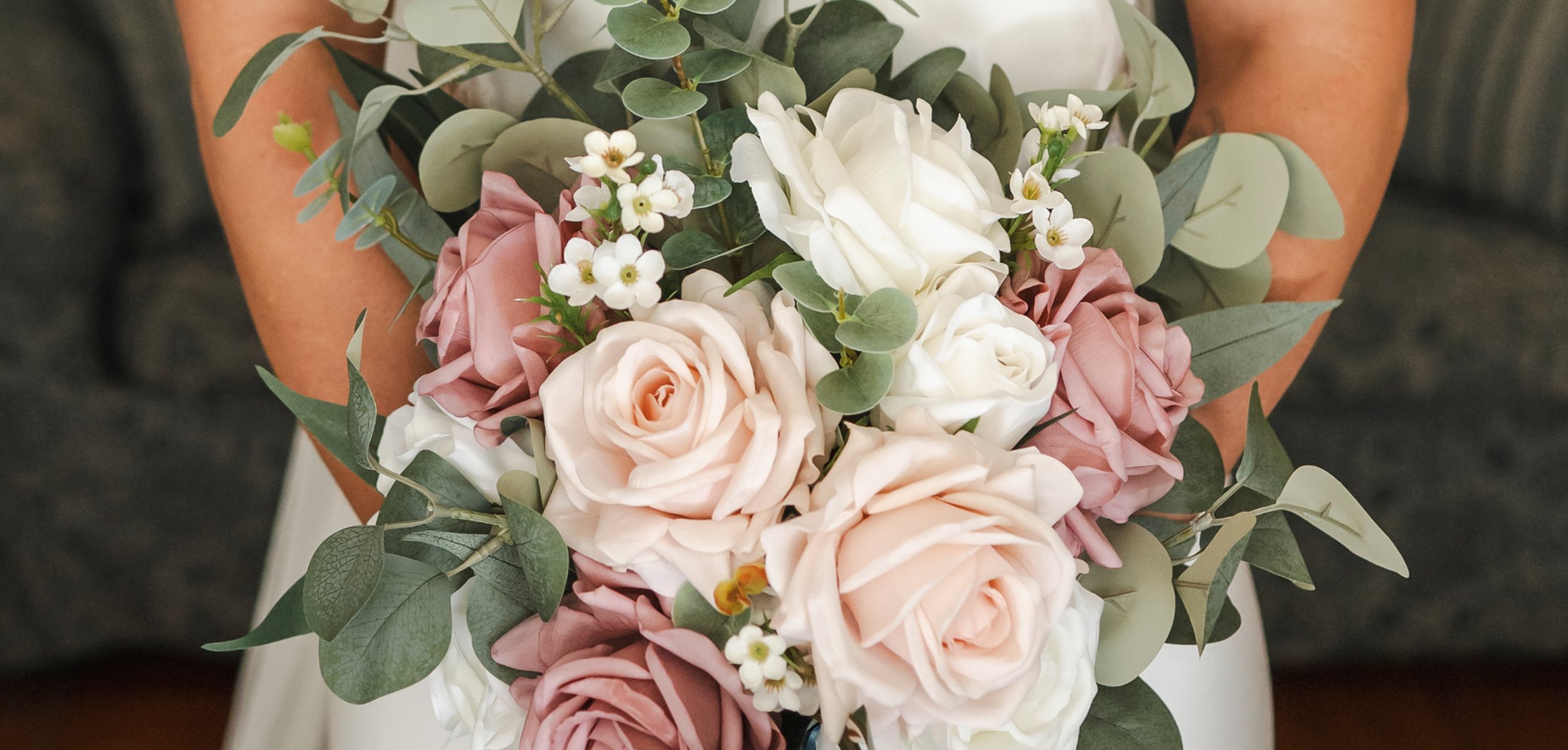 Close-up of a person's hands holding a bouquet of pale pink, white, and cream roses, with small white flowers and greenery.