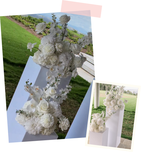 White floral arrangement with roses and orchids on a white pedestal outdoors