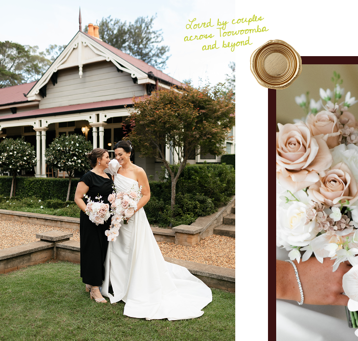 Two women, one in a white wedding gown and the other in a black dress, smiling and holding bouquets in front of a house with a red roof and garden, during a wedding celebration.