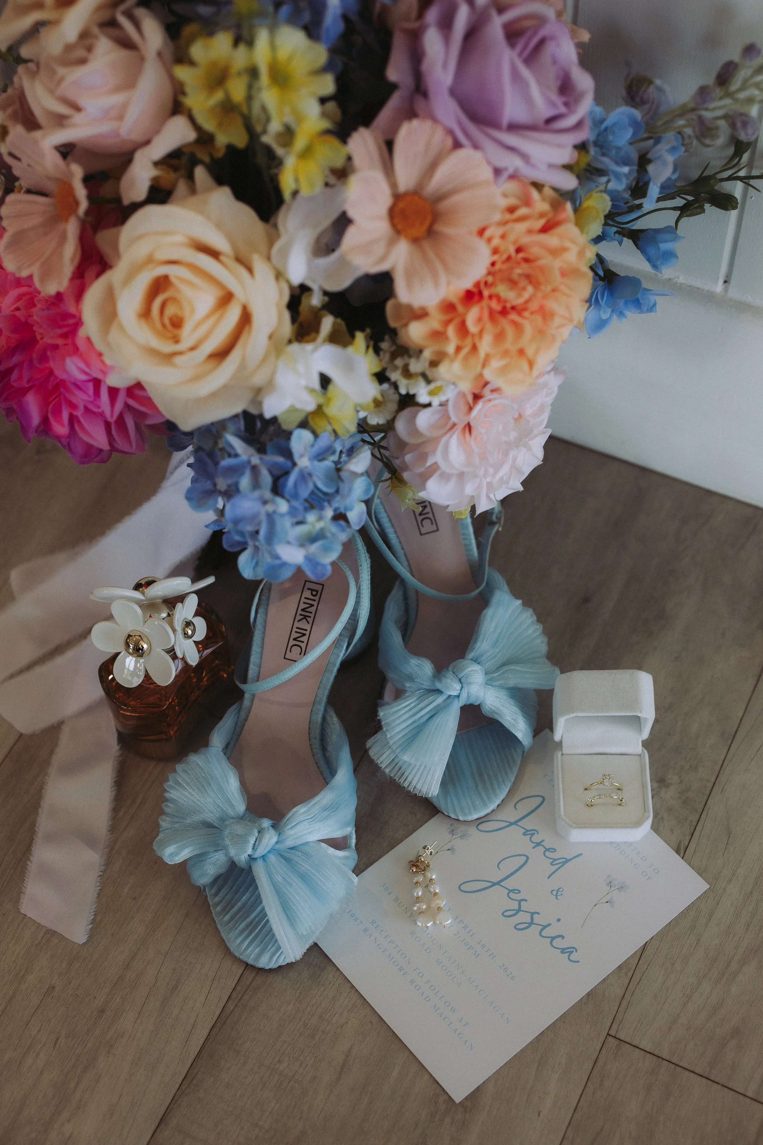 A floral display with various colorful flowers, wedding rings in a box, and jewelry on a table, possibly for a wedding or special occasion.