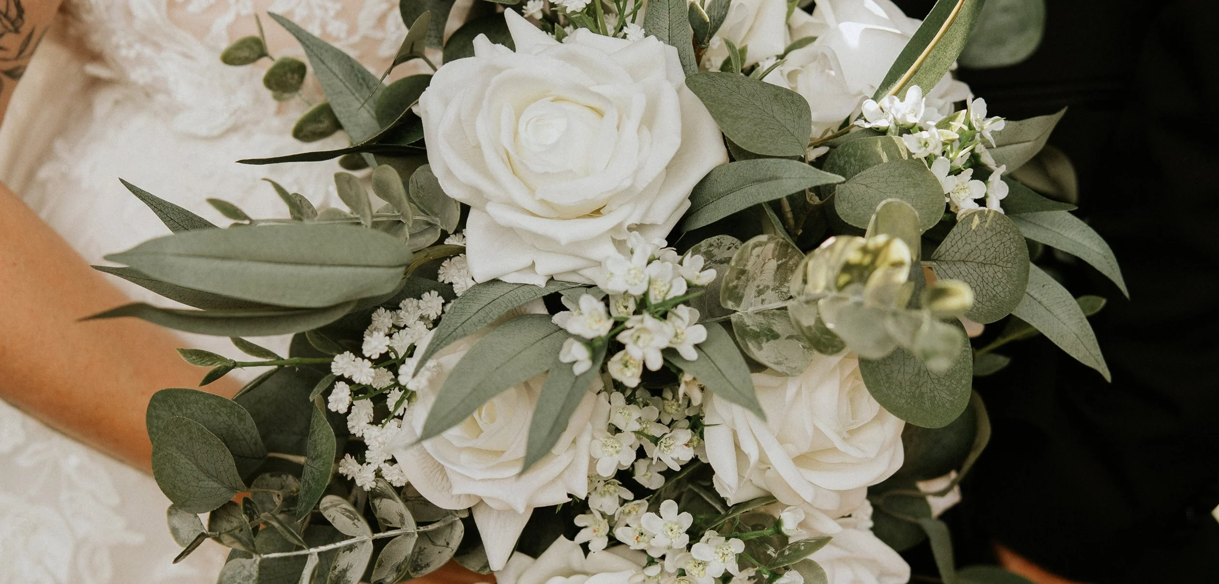 A bouquet of white roses, small white flowers, and green leaves.