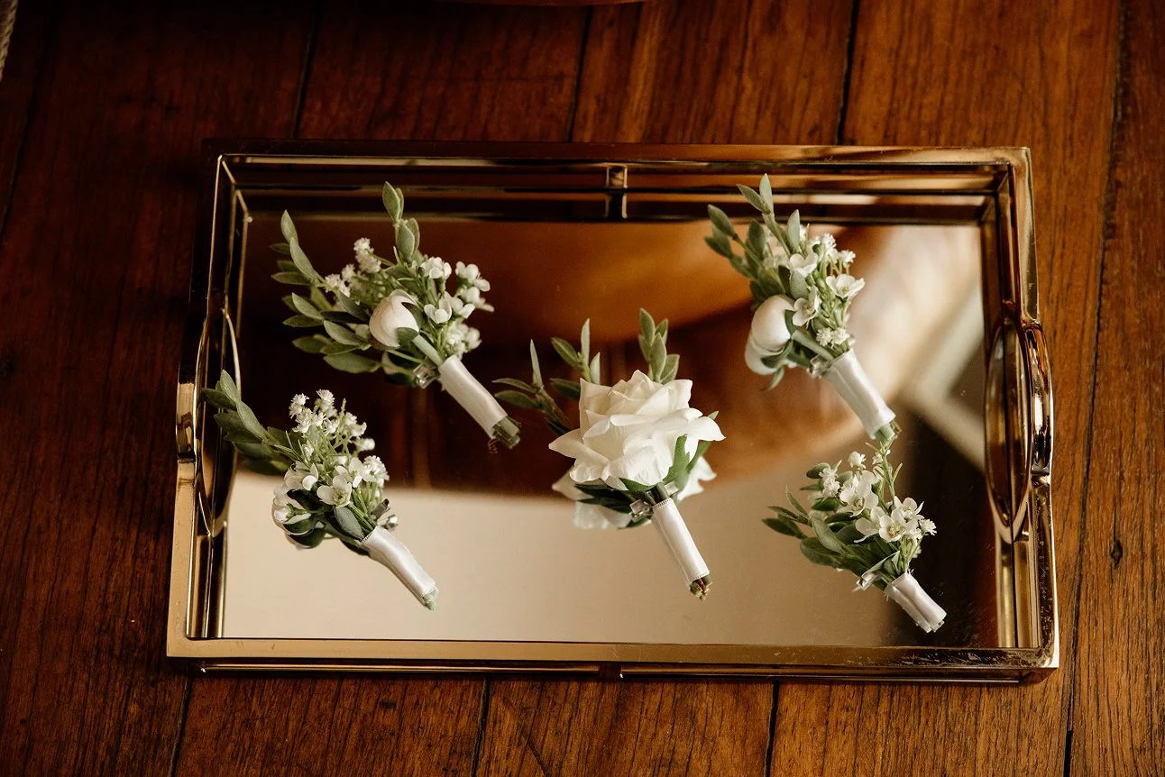 Mirror tray with five white boutonniere floral arrangements on a wooden surface.