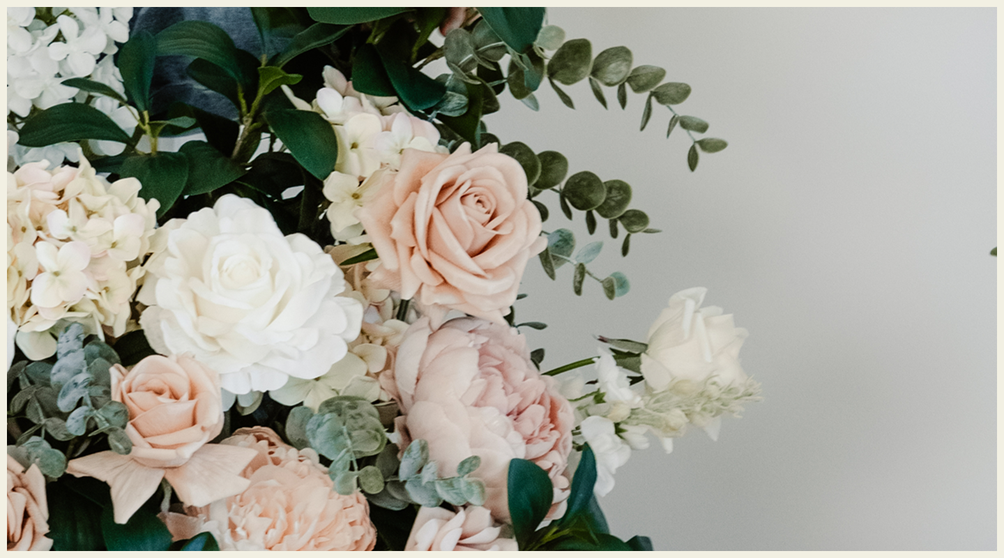 A floral arrangement with peach, white, and pink roses, along with white hydrangeas and greenery, against a plain background.