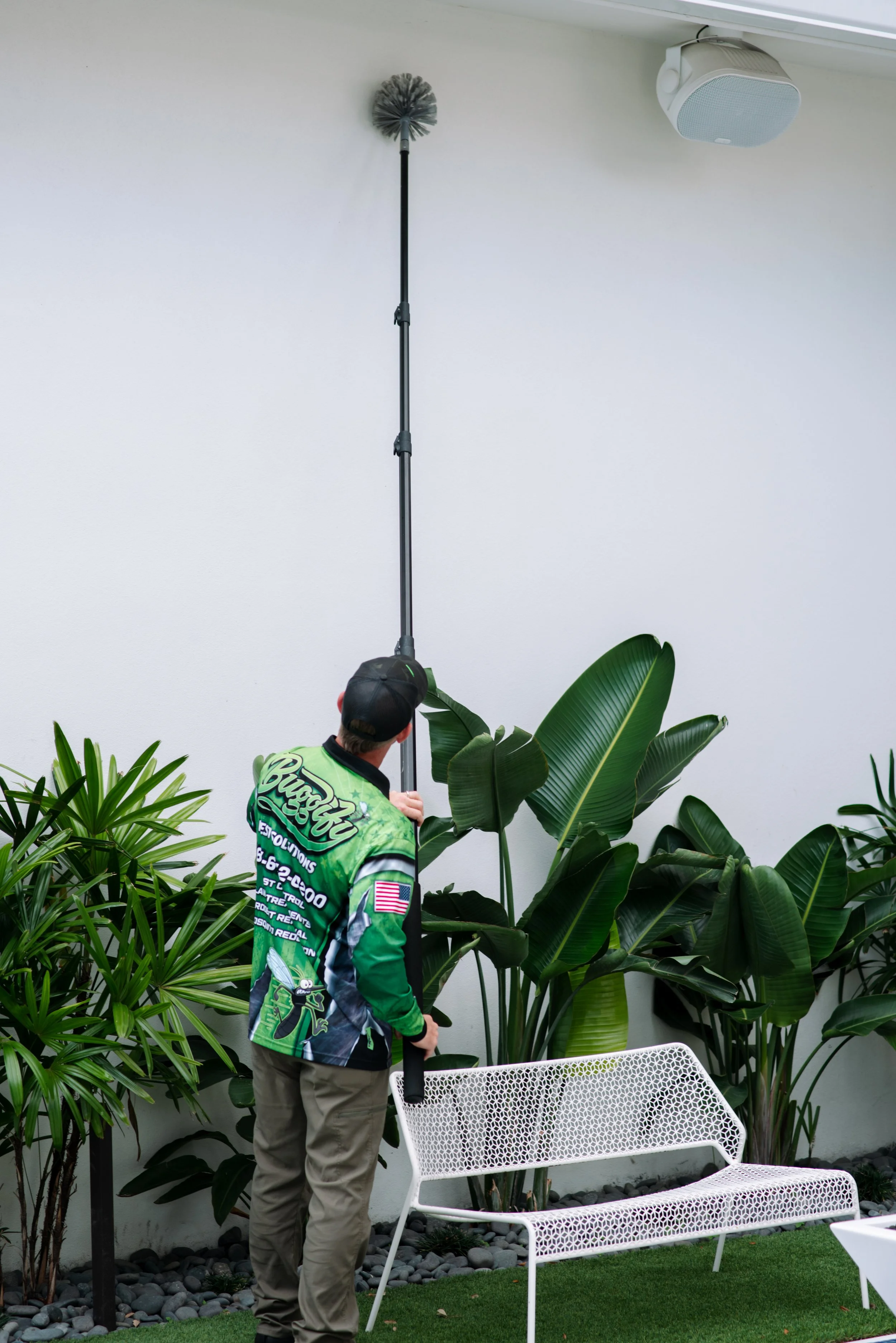 Person filming with a long boom microphone in an indoor lounge area with white chairs, green plants, and decorative rocks.