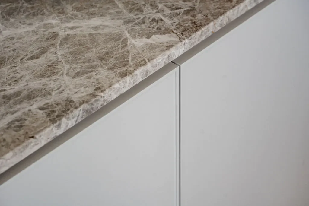 Close-up of a marble countertop edge on white cabinetry.