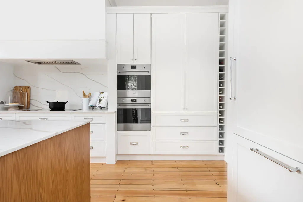 Modern kitchen with white cabinets, stainless steel appliances, a marble backsplash, and wooden flooring.
