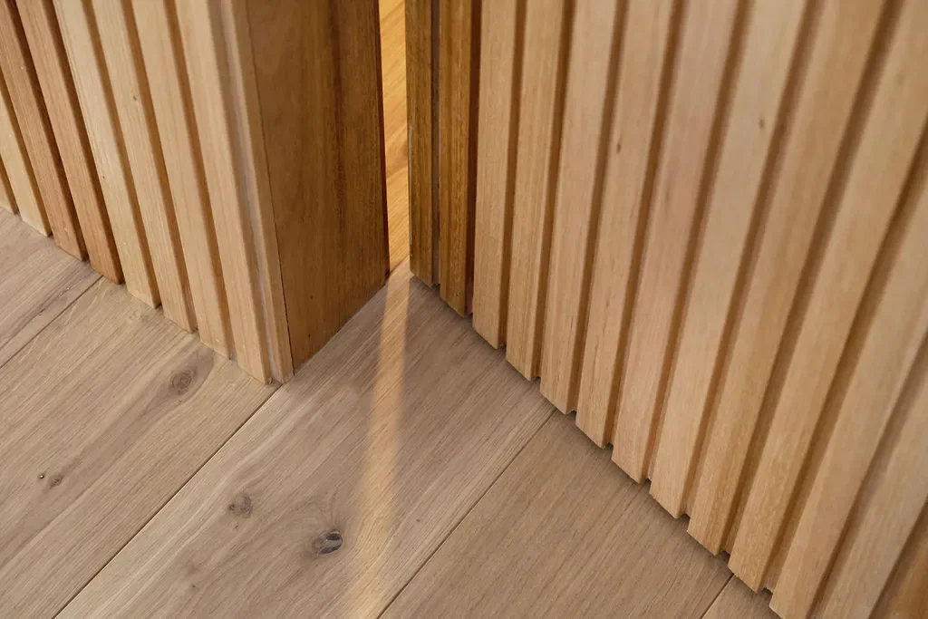 Wooden slats on wall and light-colored wooden floor with a shadow.