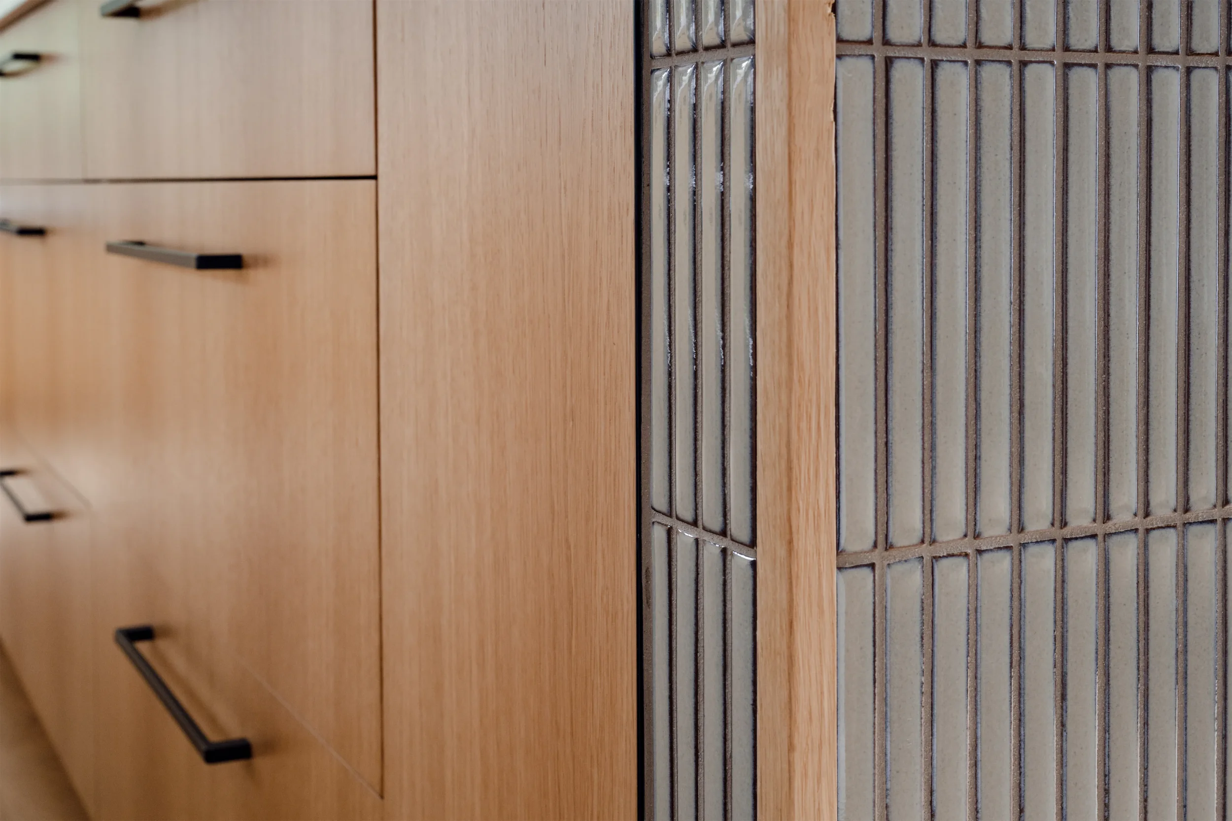 A close-up of a wooden front panel with black handles, part of a piece of furniture or cabinet, and a metal vent or grill on a wooden surface.