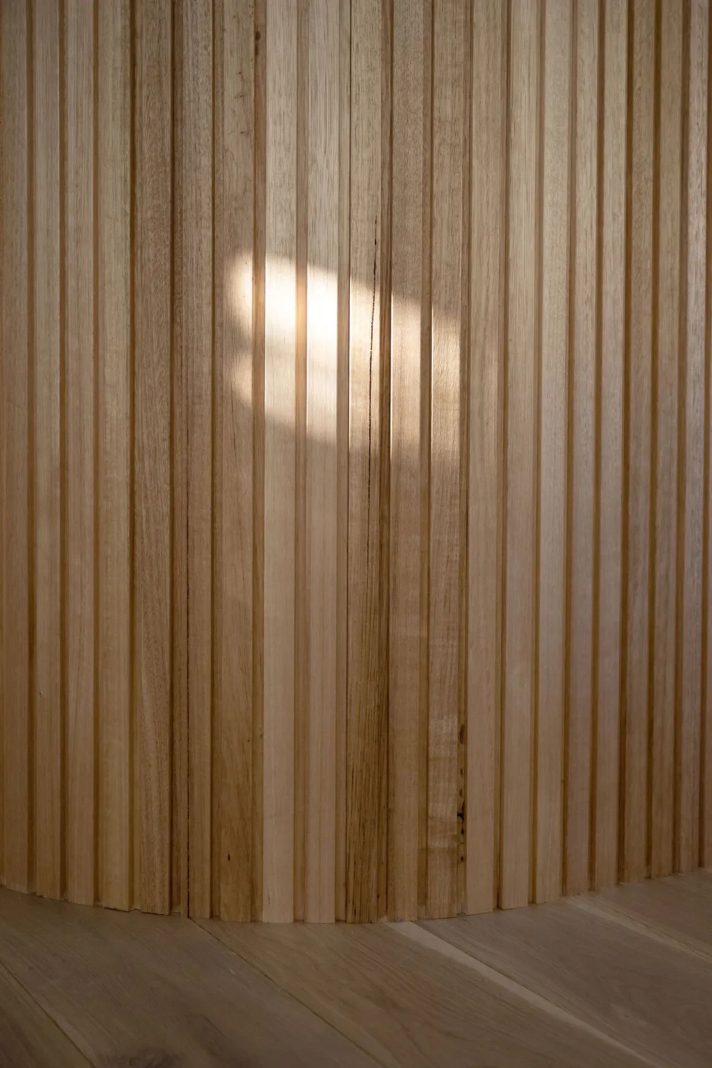Photo of a wooden wall with vertical slats and sunlight reflecting on it.