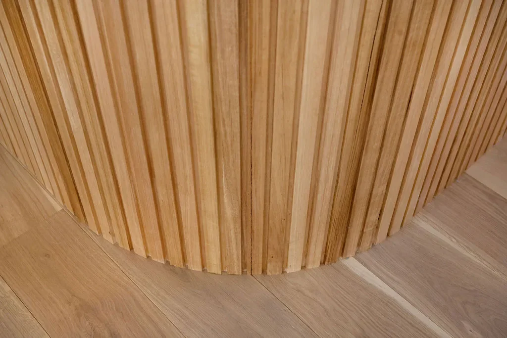 Close-up of a curved wooden wall with vertical wooden slats and a wooden floor underneath.