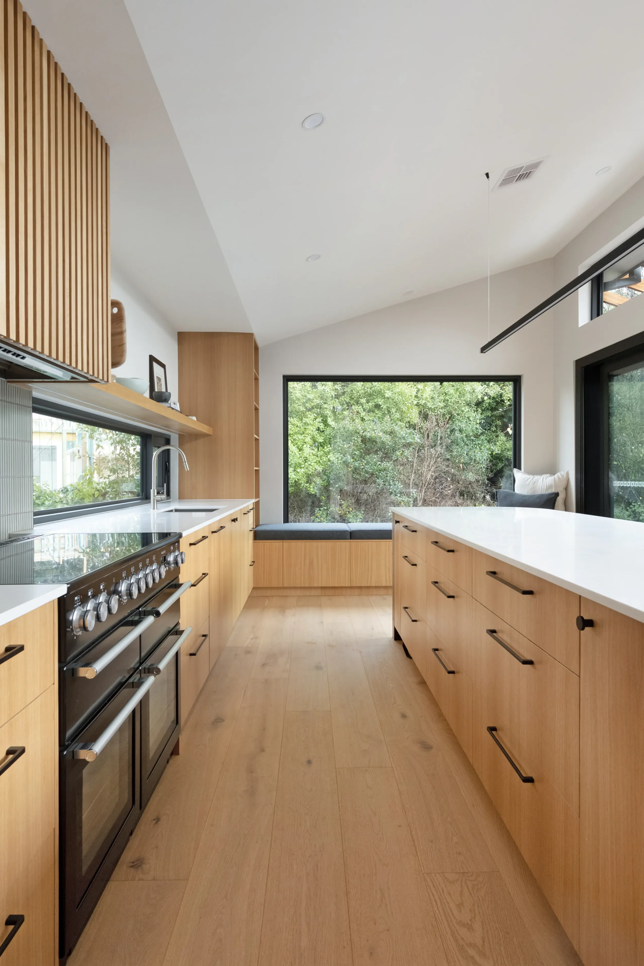 Modern kitchen with wooden cabinets, a large window with greenery outside, a gourmet stove, and a white countertop