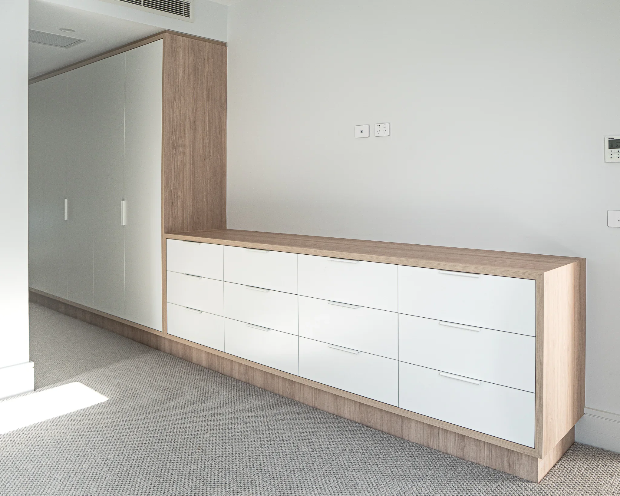 Modern built-in white cabinet with wooden accents in a room with gray carpet and a plain white wall.