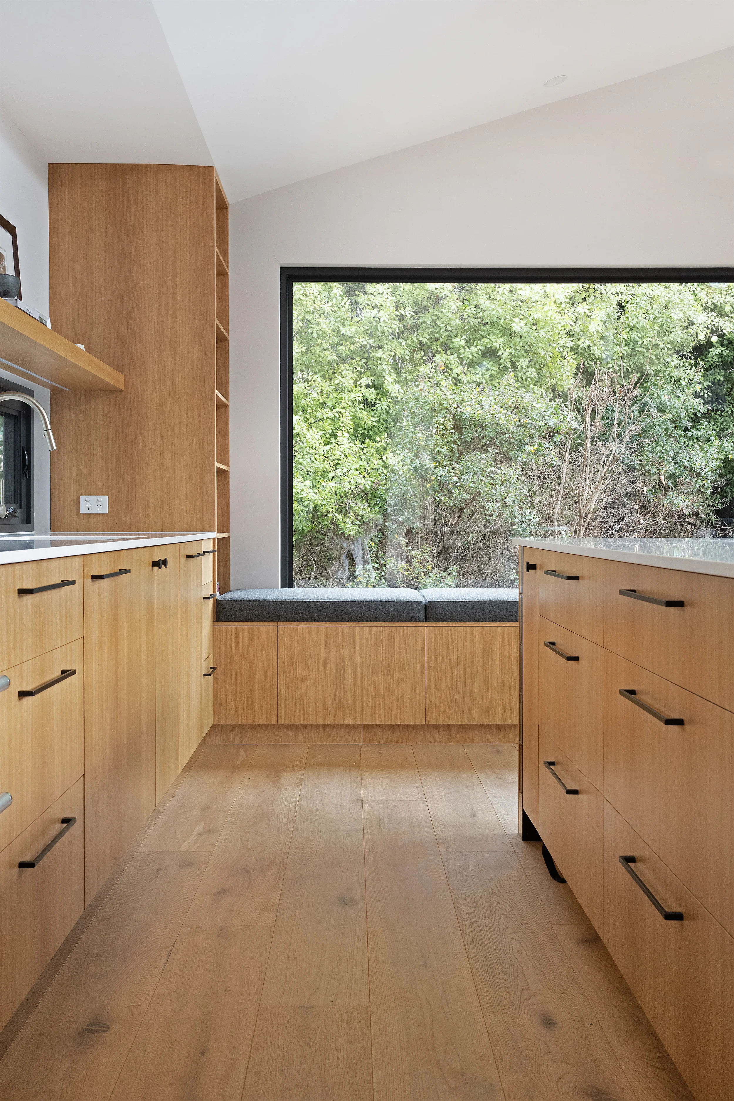 Kitchen with wooden cabinets, a large window showing green foliage outside, and a built-in bench seat under the window.