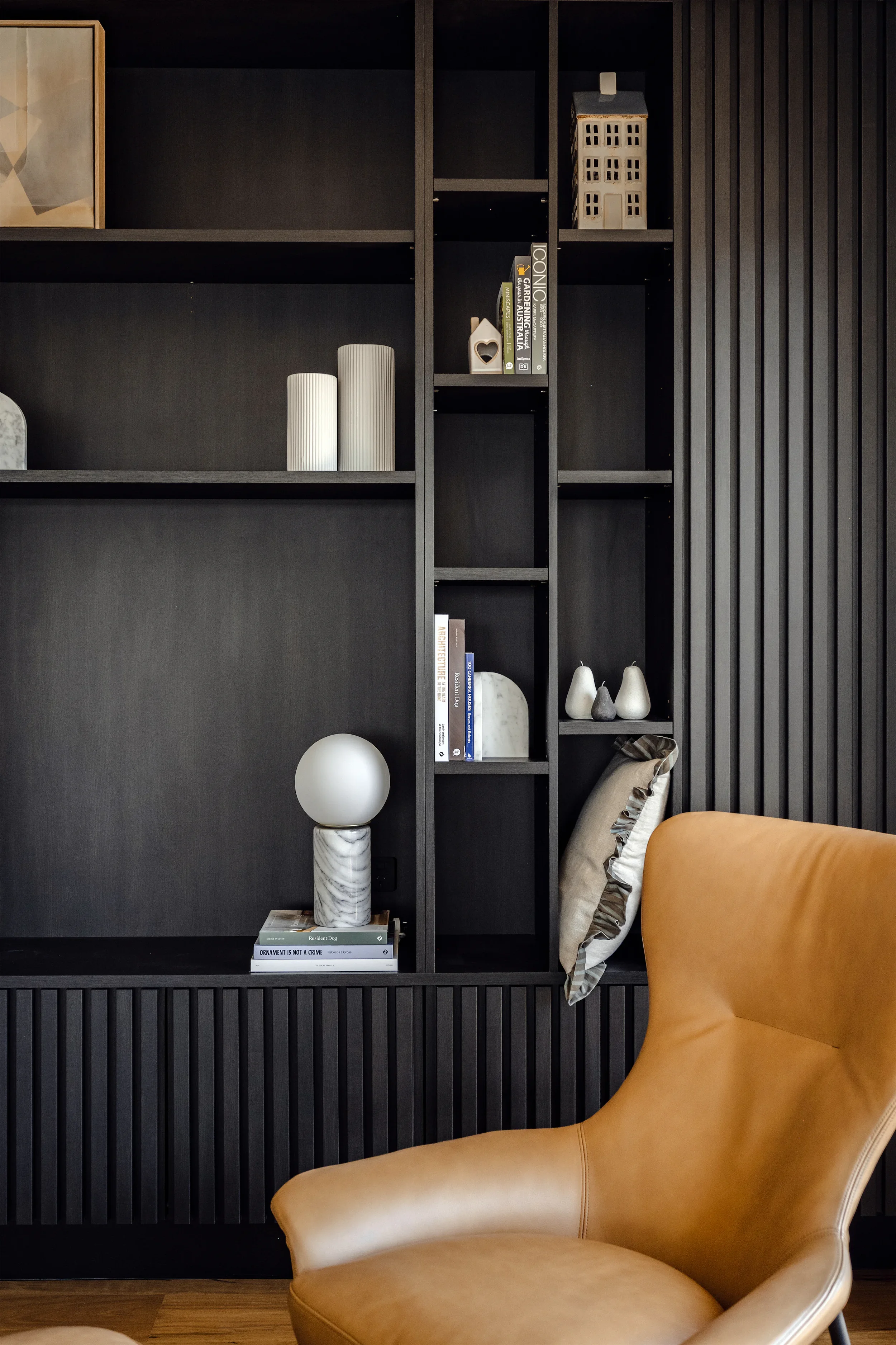 A black bookshelf with decorative items and books, next to an orange armchair in a modern interior.