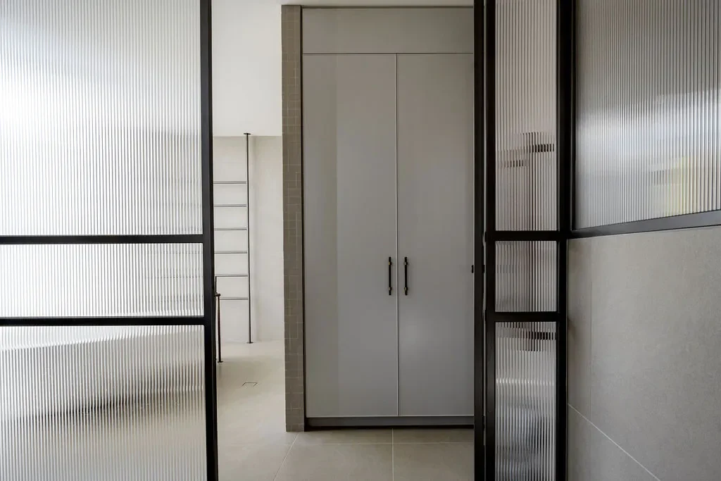 Interior view of a modern building with frosted glass partitions, a white cabinet, and a small section of a staircase.